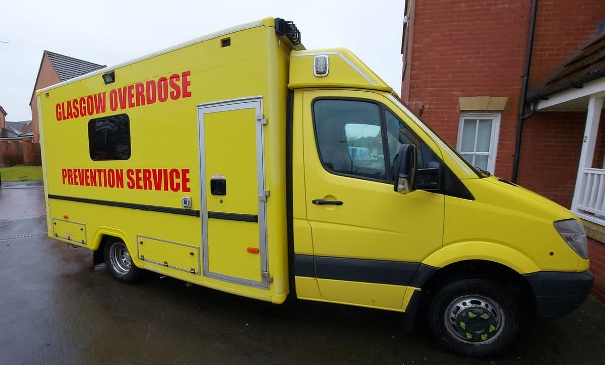 Image of Peter Krykant's yellow ambulance parked outside with the words "Glasgow Overdose Prevention Service" across the side in red.